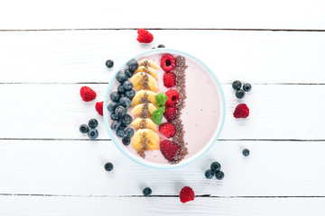 Naklejka na ściany i meble Yogurt with blueberries, raspberries and banana. In the plate. On a wooden background. Top view. Free space for text.
