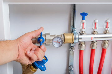 The man's hand closes the ball valve on the supply pipe of the collector for the warm floor