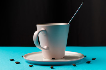 Coffee cup with spoon on saucer and coffee beans against blue background forming clock dial. Coffee as symbol of morning energy and cheerfulness or evening refreshment. Concept