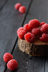 Fresh and sweet berries. Heap of raspberries on wood slab on black wooden background