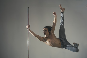 Young strong pole dancer man on pylon. grey background.