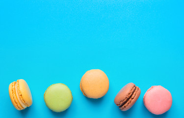 Variety of Multicolored Pink Green Yellow Brown Mocha Coffee Macarons Scattered on Blue Background Bottom Border. Bakery Confectionery Pastry Shop Poster Banner Template. Recipe Menu Mock Up