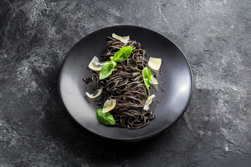 Black pasta (squid ink) with lemon pepper sauce, basil leaves, parmesan  in a black plate on a dark background. Flat top view.