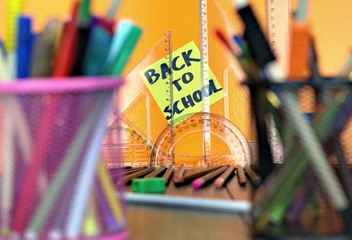 Close-up of school supplies on an orange background and the inscription back to school.