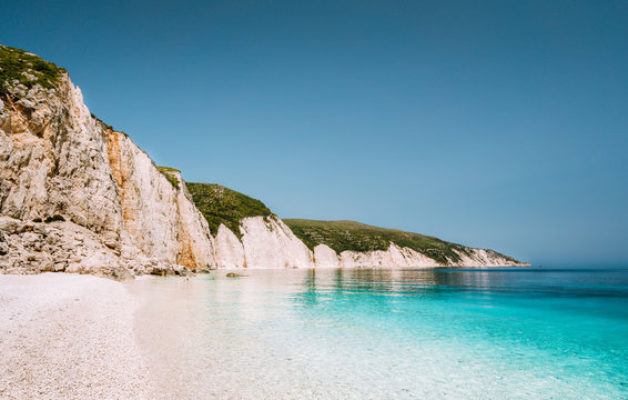 Fototapeta Fteri beach in Kefalonia Island, Greece. One of the most beautiful untouched pebble beach with pure azure emerald sea water surrounded by high white rocky cliffs of Kefalonia