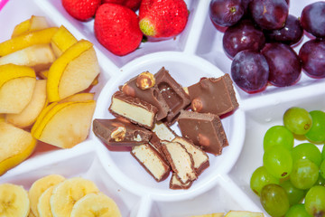 Fruit plate on a white background. Fruit and chocolate. Strawberry, banana, chocolate, grapes, apple, pear.