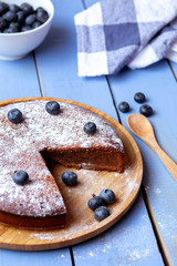 Soft chocolate cake with blueberry on a blue table with a blue and white checkered dish towel and a wooden spoon