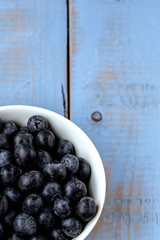 Macro photography of a white bowl full of blueberry on a blue wooden table