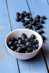 Macro photography of a white bowl full of blueberry on a blue wooden table