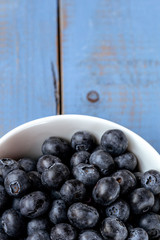 Macro photography of a white bowl full of blueberry on a blue wooden table