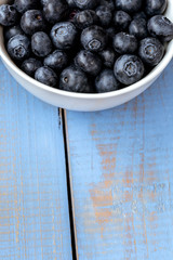 Macro photography of a white bowl full of blueberry on a blue wooden table