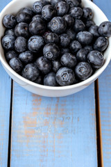 Macro photography of a white bowl full of blueberry on a blue wooden table