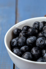 Macro photography of a white bowl full of blueberry on a blue wooden table