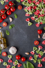Obraz na płótnie Canvas Pasta farfalle, cherry tomatoes, garlic, olive oil and basil on dark background with copy space