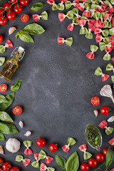 Pasta farfalle, cherry tomatoes, garlic, olive oil and basil on dark background with copy space