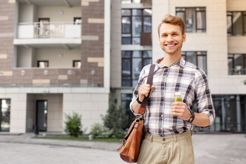 Great mood. Happy joyful man smiling while holding a bottle of smoothie