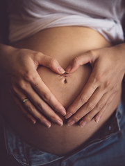 woman's hands in heart-shaped gesture laying on pregnant belly