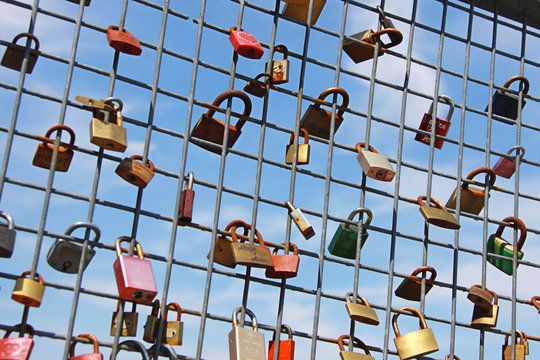 collection of love & friendship padlocks mounted on a grate against blue sky