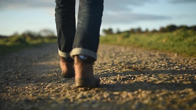 Man in hiking boots and jeans walking along a dirt path. Sunrise or sunset.