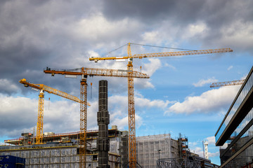 Yellow cranes over building with dramatic clouds in background