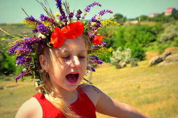 Little girl on her head with a wreath of flowers in nature in summer.