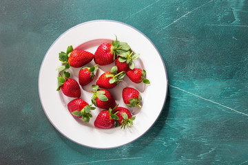 Fresh strawberries in olive wooden plate on blue background, copy space. Top view