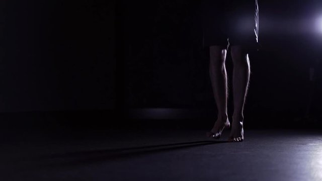 Man s legs in shorts skipping rope in a dark gym. Cardio workout and boxing. Concept of a healthy lifestyle. Left to right pan slow motion medium shot