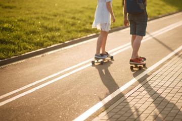 Happy young couple having fun with skateboard on the road. Young man and woman skating together on a sunny day.