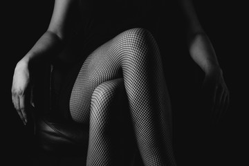 Girl in black fishnet stockings against dark background. Sexy woman in stockings sitting on chair. Strict woman domination bdsm concept.