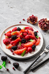Salad with berries (blackberries and raspberries), grapefruit and pomegranate seeds on grey background. 