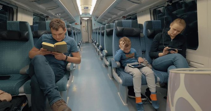 Cinemagraph - Parents with child traveling by express train at night. Father reading book while mother and son using mobile and tablet computer
