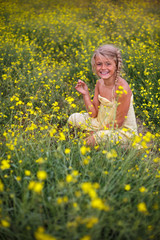 Naklejka na ściany i meble Portrait of happy little girl in field of yellow blossoming arugula. Travel and recreation