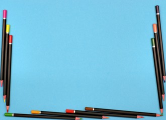 Frame with colorful crayons on a blue background and copy space.