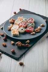 Traditional oriental sweets and nuts: hazelnuts, cashews on a white wooden background. Turkish dessert is the locus of Rahat. View from above. Place under the text.