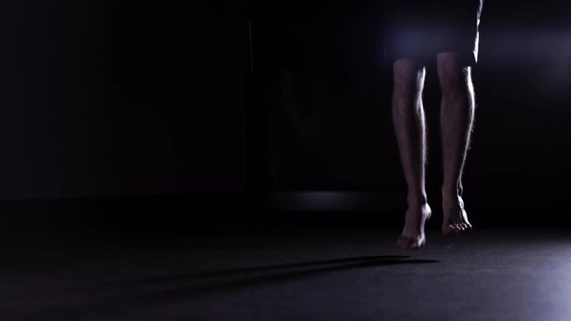 Man s legs in shorts skipping rope in a dark gym. Cardio workout and boxing. Concept of a healthy lifestyle. Right to left pan real time medium shot
