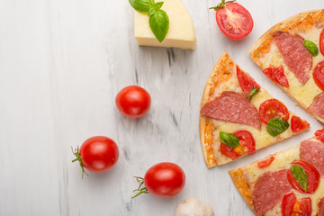Delicious sliced pizza with tomatoes, mozzarella cheese, basil, and a tomato on a light background,
