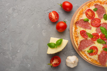 Food ingredients and spices for cooking mazarella cheese, cherry tomatoes, garlic, basil and delicious Italian pizza on a gray concrete background. Copyspace. View from above. banner