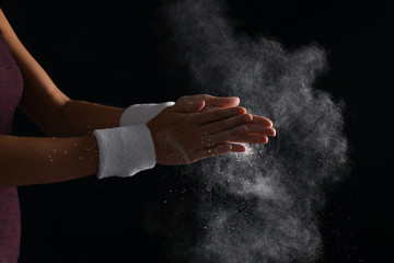 Young woman applying chalk powder on hands against dark background