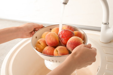 Woman washing fresh sweet peaches in kitchen