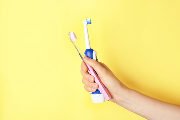 Woman holding manual and electric toothbrushes against color background
