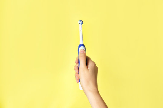 Woman holding electric toothbrush against color background