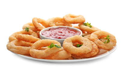 Plate with fried onion rings and bowl of sauce on white background