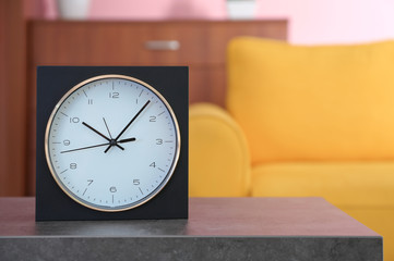 Stylish clock on table against blurred background. Time of day