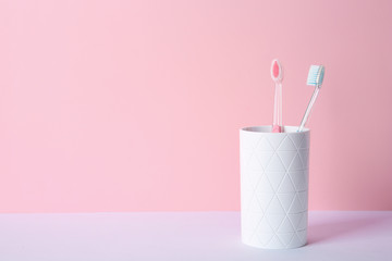 Cup with toothbrushes on table against color background. Dental care