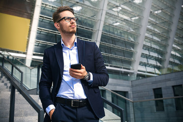 Business man stand at street holding a smartphone in office park