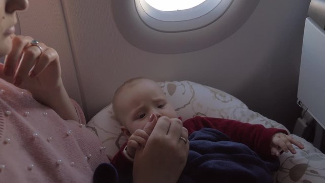 Baby girl traveling by plane with mum. Child lying on mothers lap and following her moving fingers