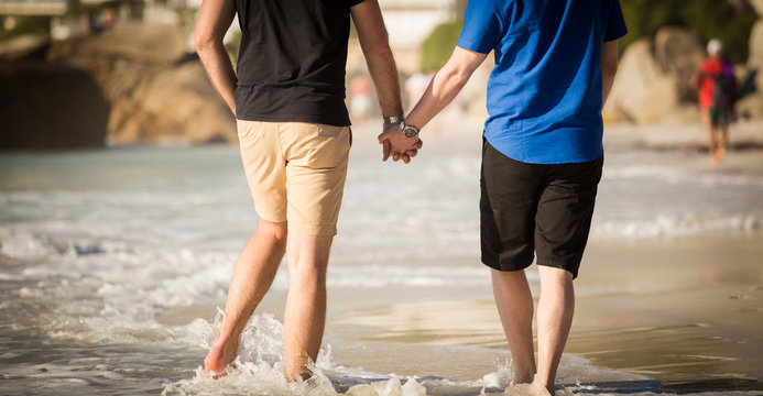 Close up image of a gay male couple holding hands on the beach in cape town south africa