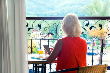 Woman sitting on balcony in early morning.Female using smartphone reads news.Vacation holiday concept.