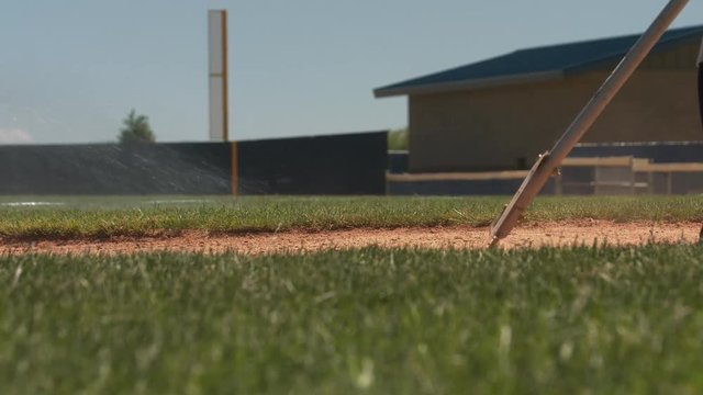 Raking the 3rd base line after baseball game. Men are fixing a baseball ground, making the ground even and flat. Another man is sprinkling water on the grass and on the ground.