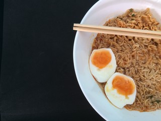 Noodles and egg  in a white bowl placed on a black table. There are chopsticks on top.